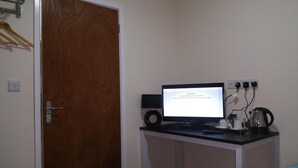 A room with a wooden door, a desk with a computer monitor, a keyboard, a mouse, and a speaker. There are power outlets on the wall and a coffee maker on the desk. - The Oxford House (Oxford)