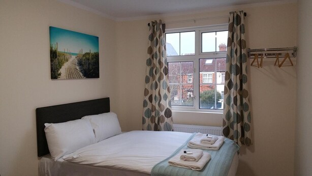 A bedroom with a bed, a window with curtains, a radiator, and a painting on the wall. - The Oxford House (Oxford)