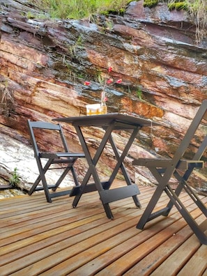 A wooden deck with a table and chairs, set against a rocky cliff backdrop. - Pousada Marotta (Ouro Preto)