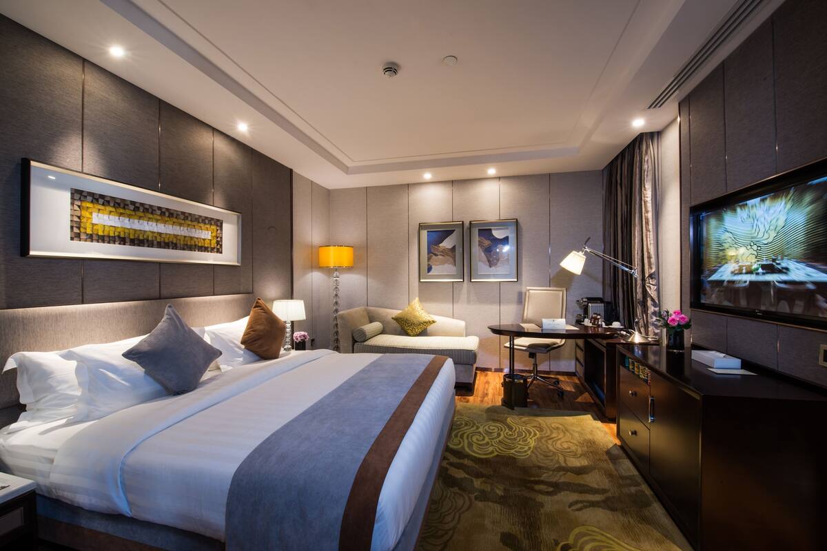 A hotel room with a large bed, a desk, a television, and a sofa.
