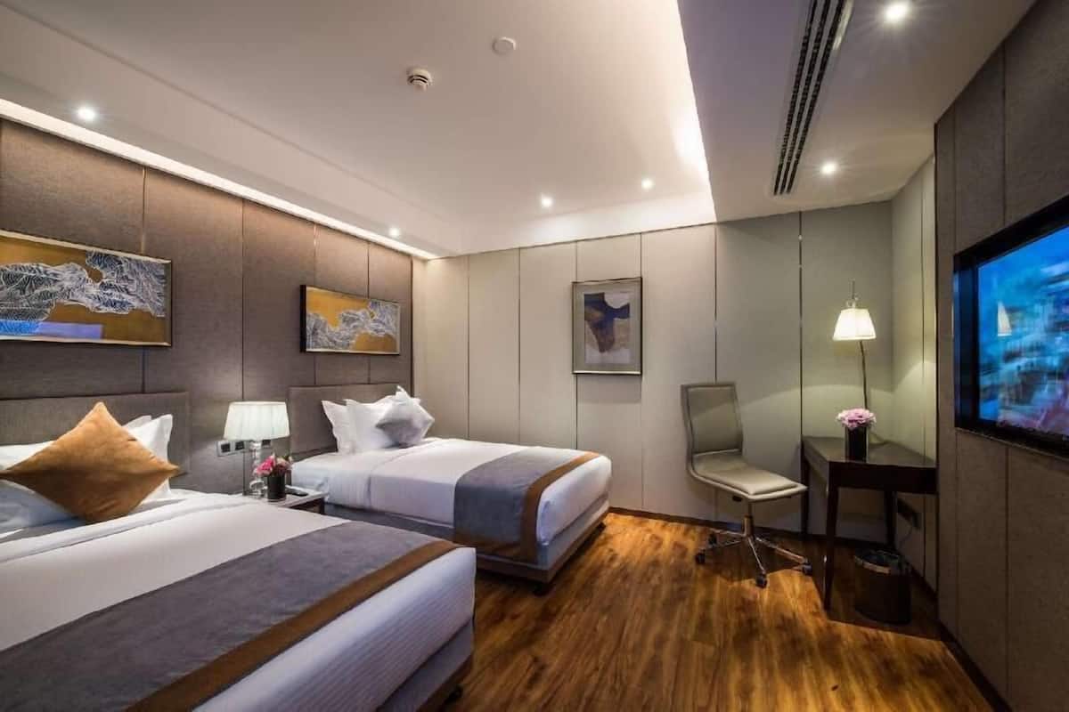 A hotel room with two beds, a desk, a chair, a TV, and artwork on the walls.