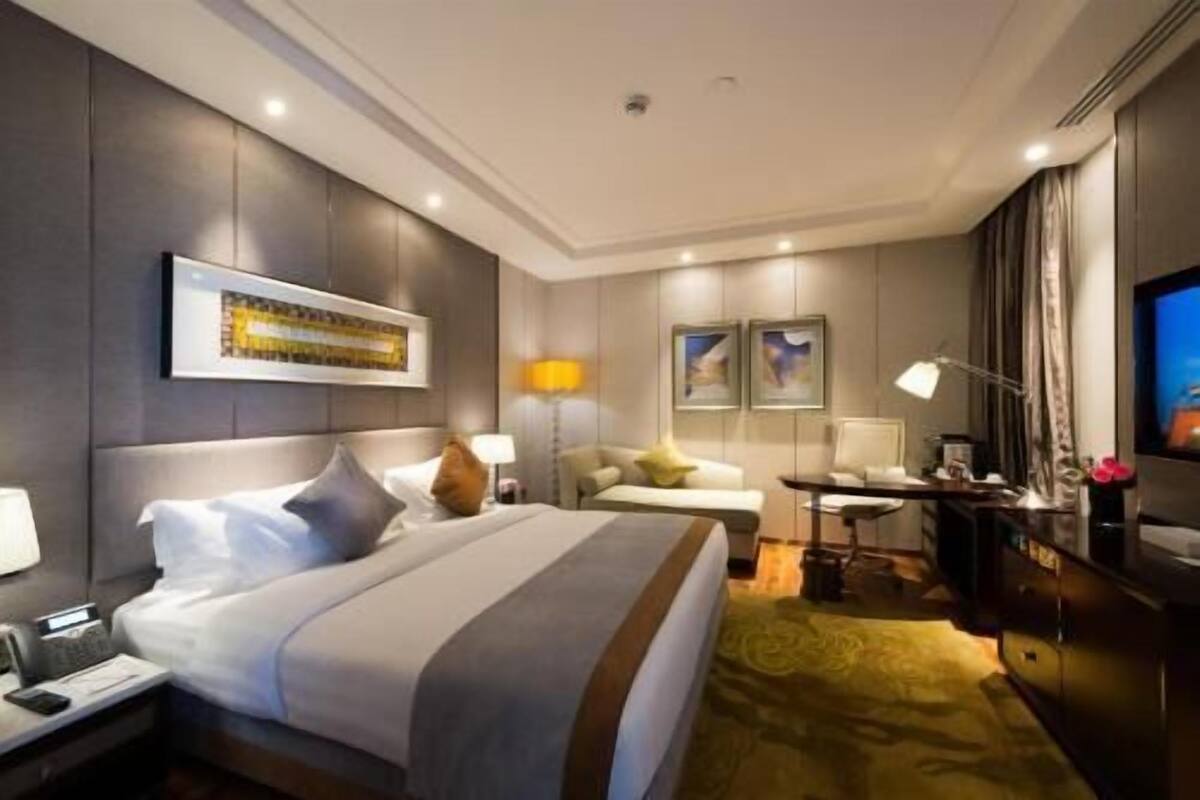 A hotel room with a large bed, bedside tables, a desk, a chair, a television, and artwork on the walls.