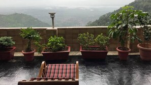 A rooftop terrace with potted plants and a wooden chair. - Norbu House (Dharamshala)