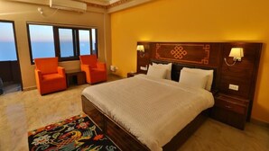 Habitación de hotel con una cama grande, dos sillones anaranjados, un cabecero decorativo y vista al océano.
