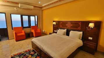 Ein Hotelzimmer mit einem großen Bett, zwei orangen Sesseln, einem dekorativen Kopfteil und Blick aufs Meer.