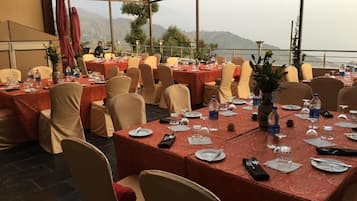 Ein Festsaal mit gedeckten Tischen für eine festliche Veranstaltung, mit Blick auf eine Berglandschaft durch große Fenster.