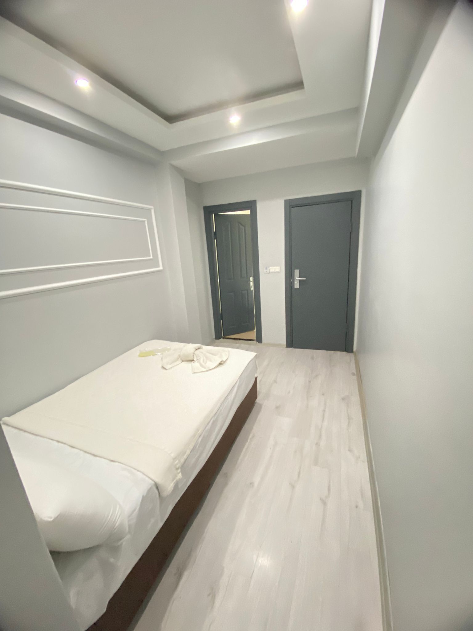 A bedroom with a single bed, a door, and a light-colored wooden floor.