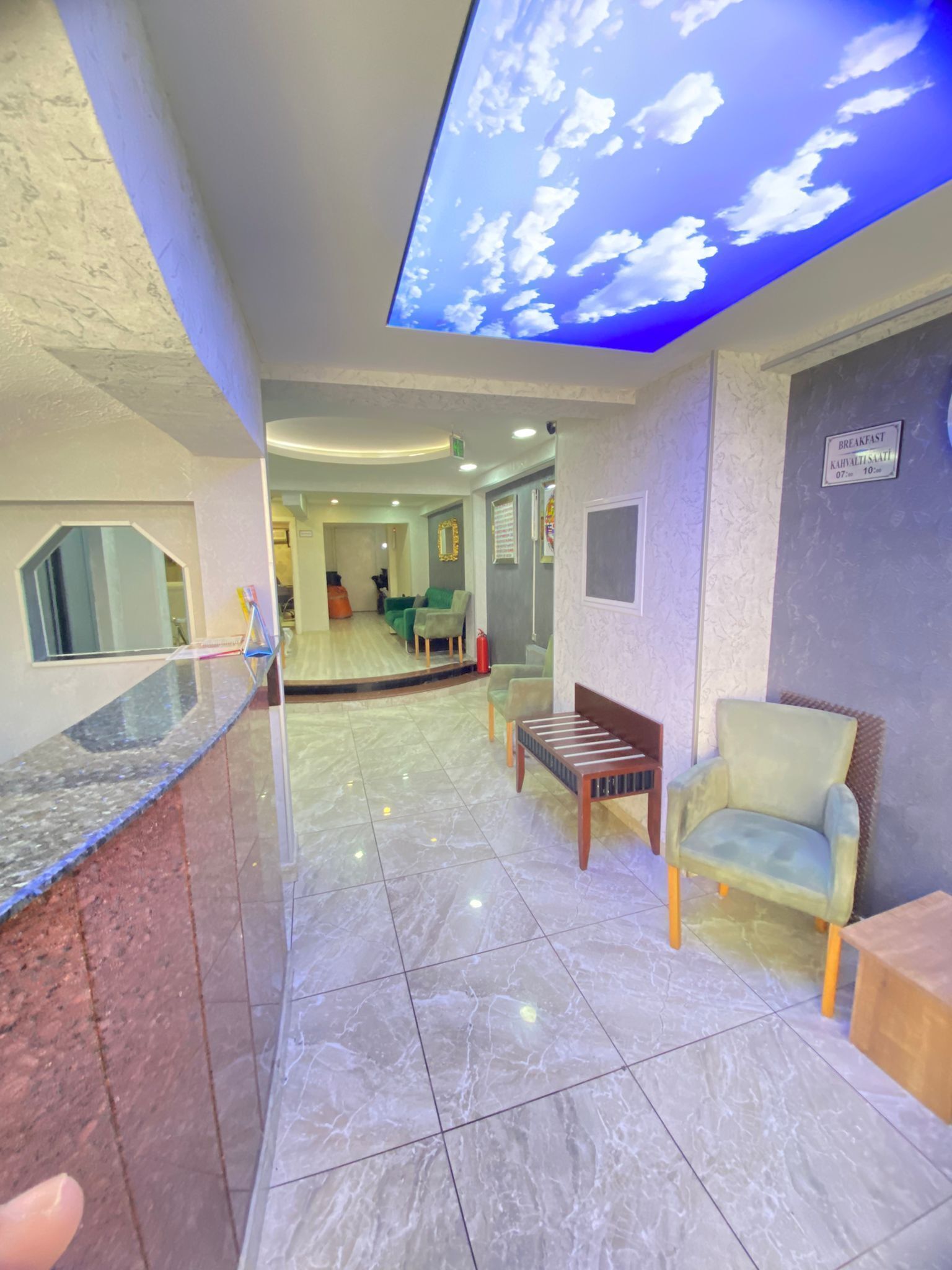 A hotel lobby with a reception desk, seating area, and a ceiling with a cloud projection.