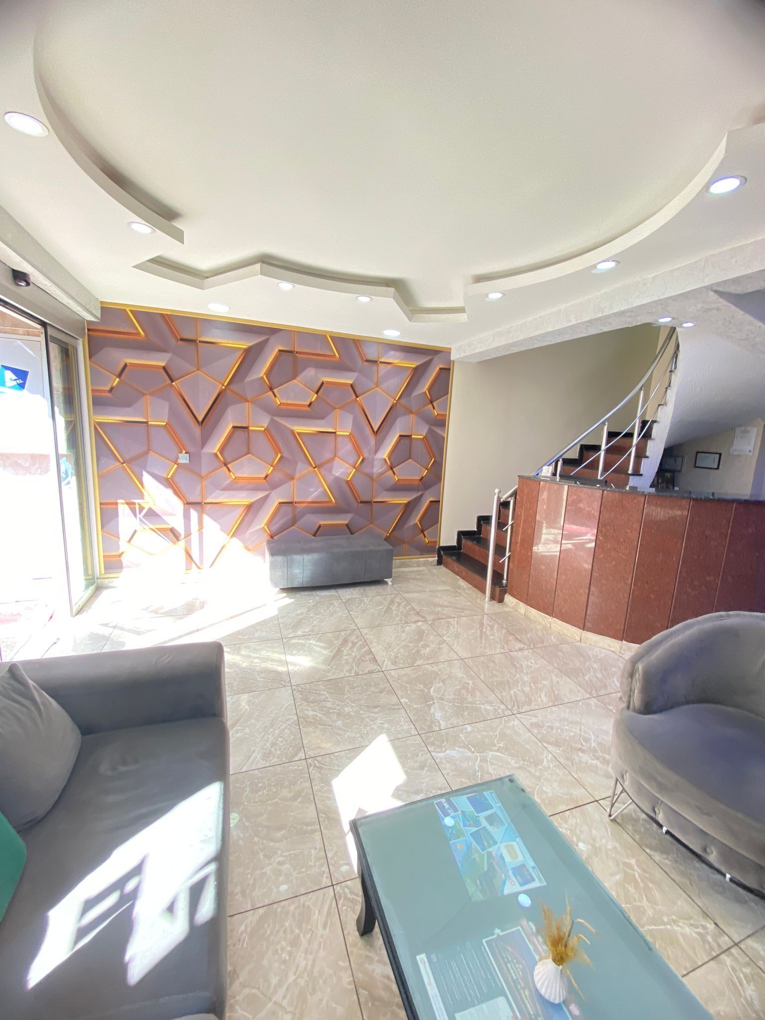 A modern lobby with a geometric patterned wall, a staircase, and a reception desk.