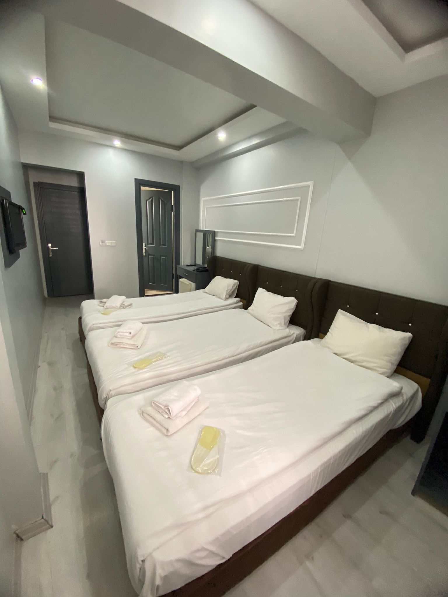 Une chambre d’hôtel avec trois lits, chacun agrémenté de serviettes soigneusement pliées et d’une bouteille de lotion.