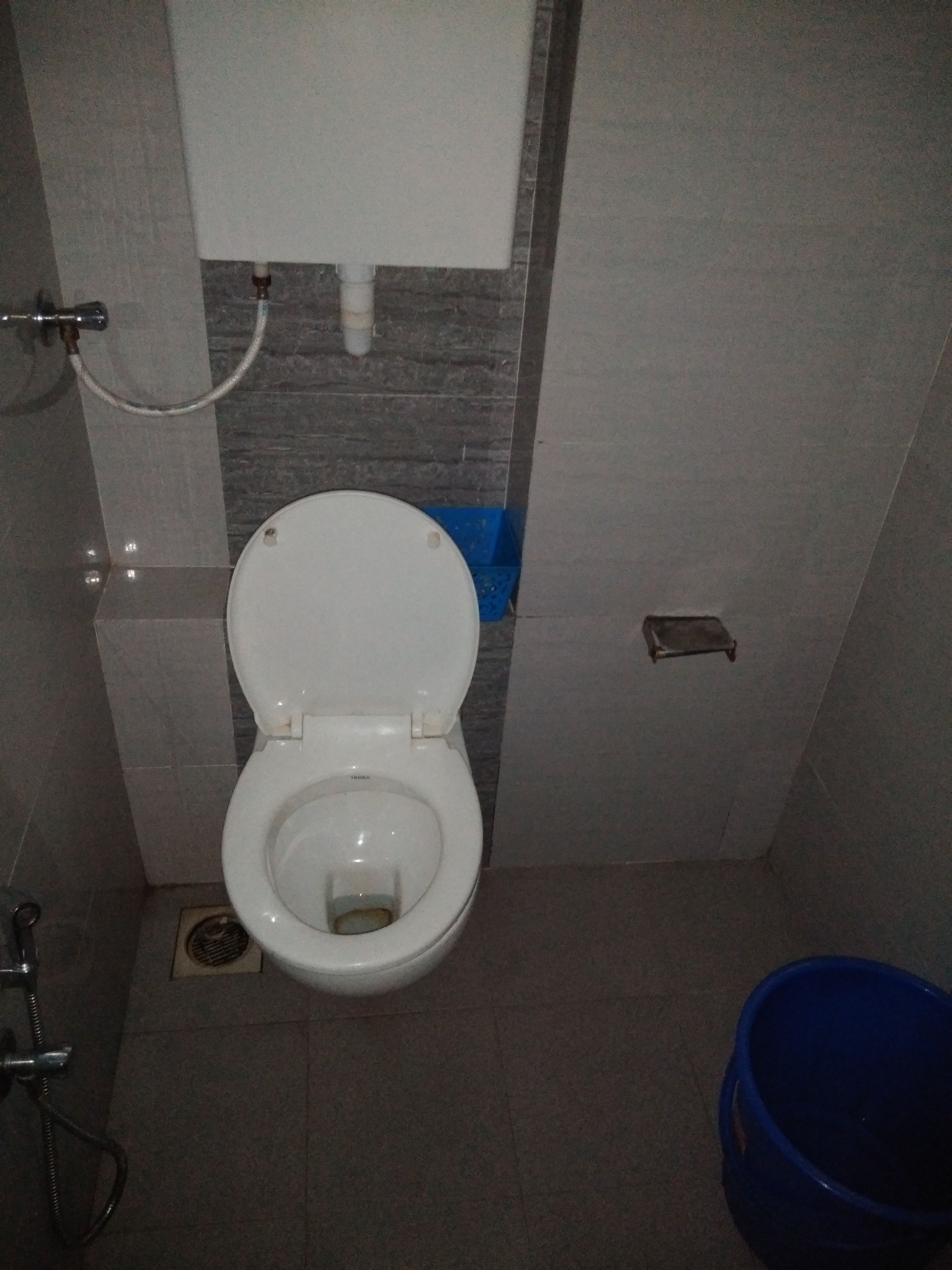 A standard bathroom with a toilet, a hand dryer, and a blue waste bin.