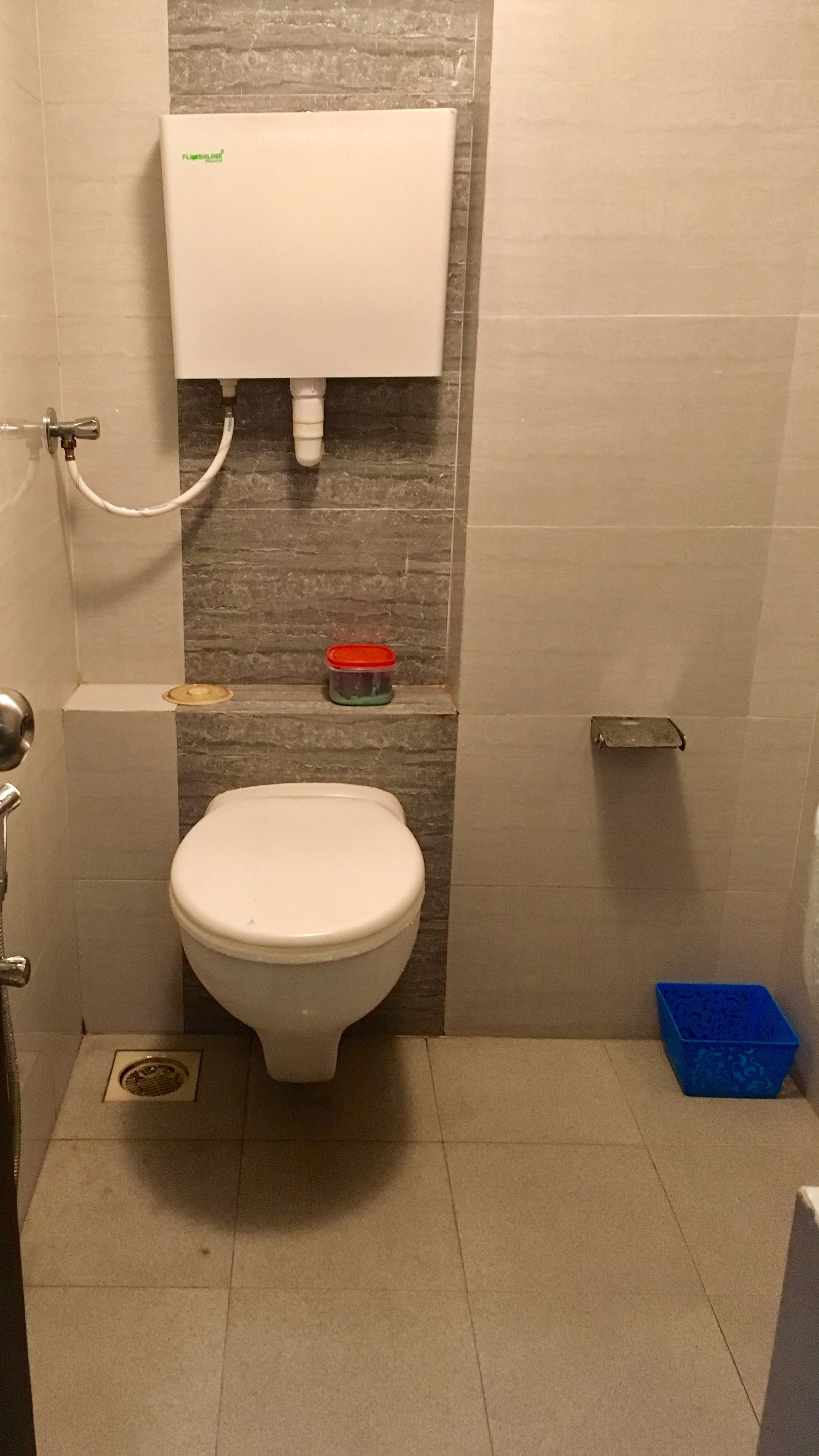 Un bagno piccolo con un water, un portasciugamani per carta igienica fissato alla parete, un soffione doccia e un cestino della spazzatura blu.