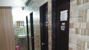 A corridor with tiled walls, a sink, and a door with a sign. - Golden Dormitory - Hostel (Mumbai)