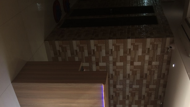 A reception area with a wooden reception desk, a tiled wall, and a view of the outside. - Golden Dormitory - Hostel (Mumbai)