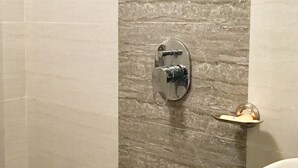 A bathroom with a stone wall, a showerhead, a sink, and a blue trash bin. - Golden Dormitory - Hostel (Mumbai)