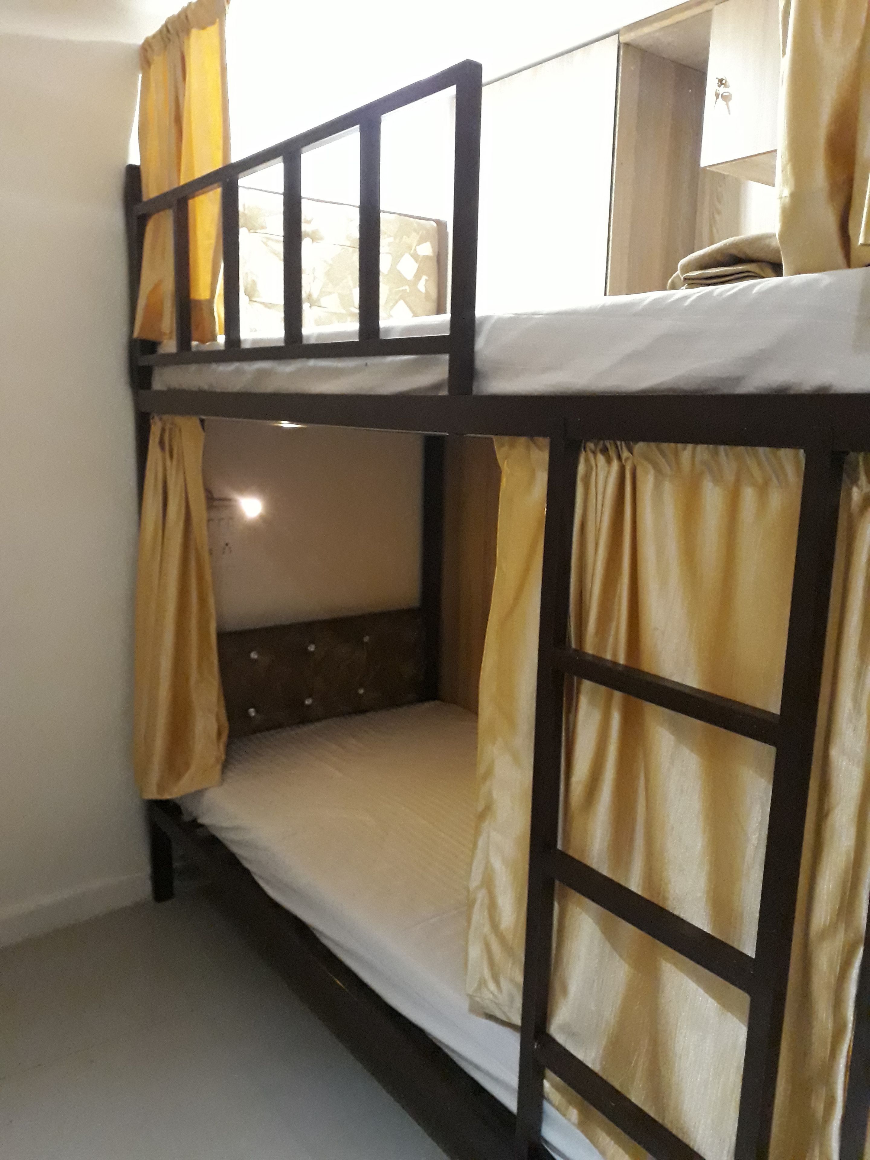 Una cama individual con cortinas amarillas, cabecera de madera y colchón blanco.