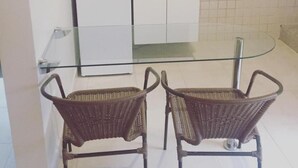 Una cuina compacta amb armaris blancs, un rentaplats integrat i una taula de dinar de vidre amb dues cadires de vimet.