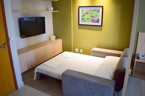 Ein Hotelzimmer mit Bett, Fernseher, Schreibtisch und einem Bild an der Wand.