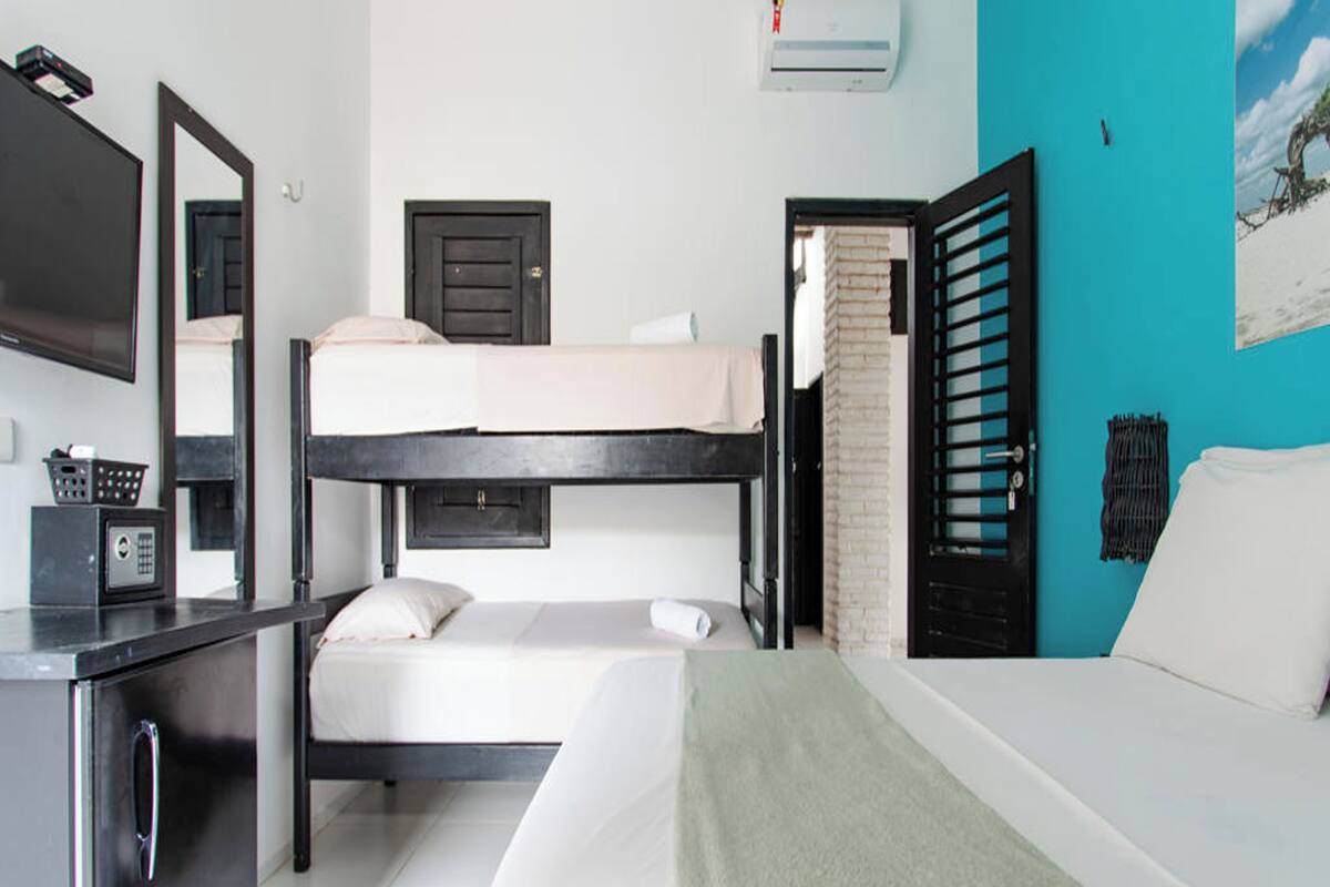 A hotel room with a bunk bed, a desk with a computer, a TV, and a window with a view of the sky.