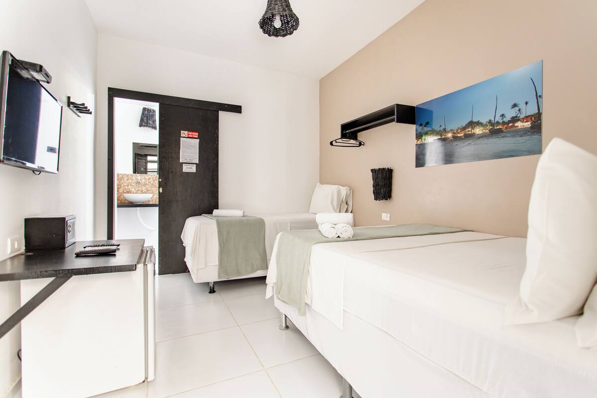 A hotel room with a bed, a desk with a computer, a TV, and a painting on the wall.