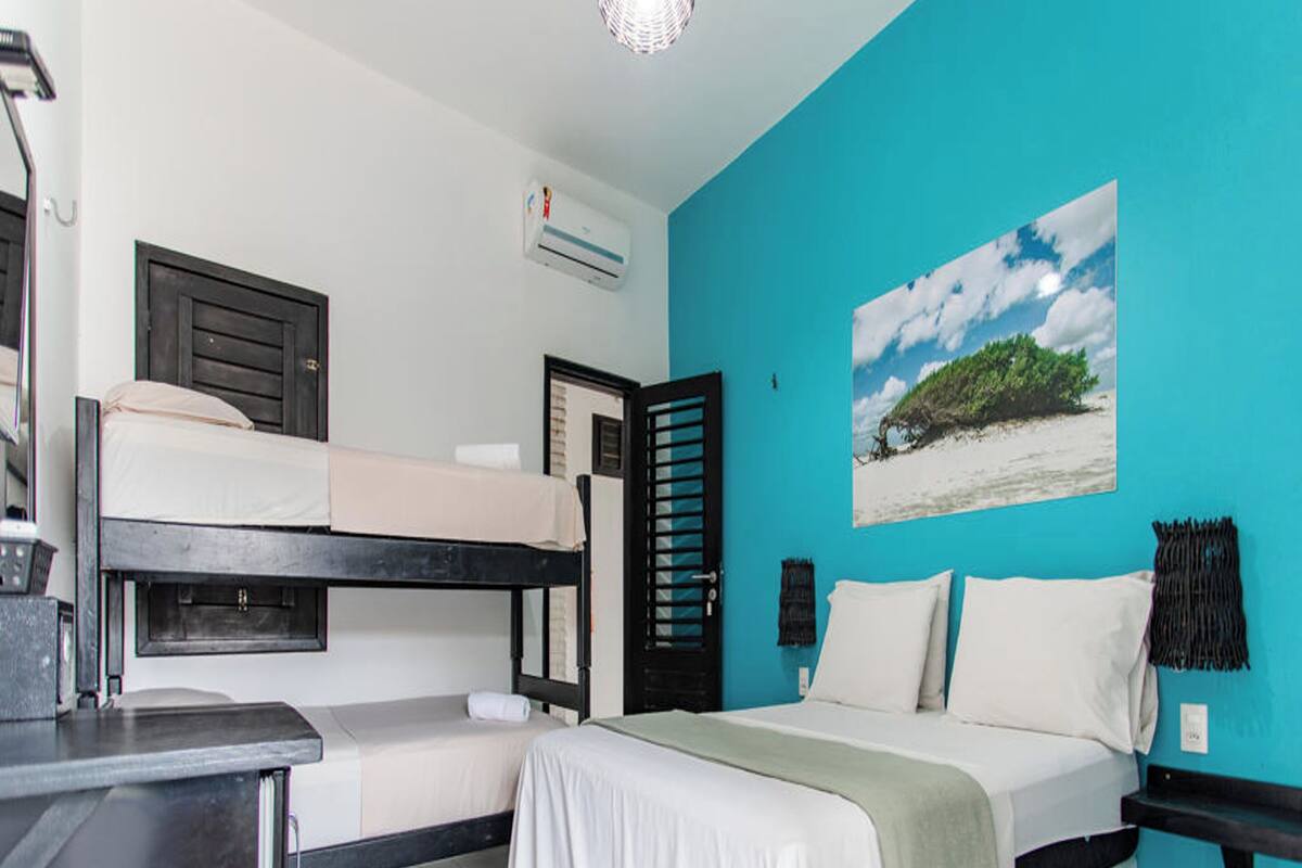 A bedroom with a bunk bed, a bed with pillows, a desk, and a wall-mounted air conditioner.