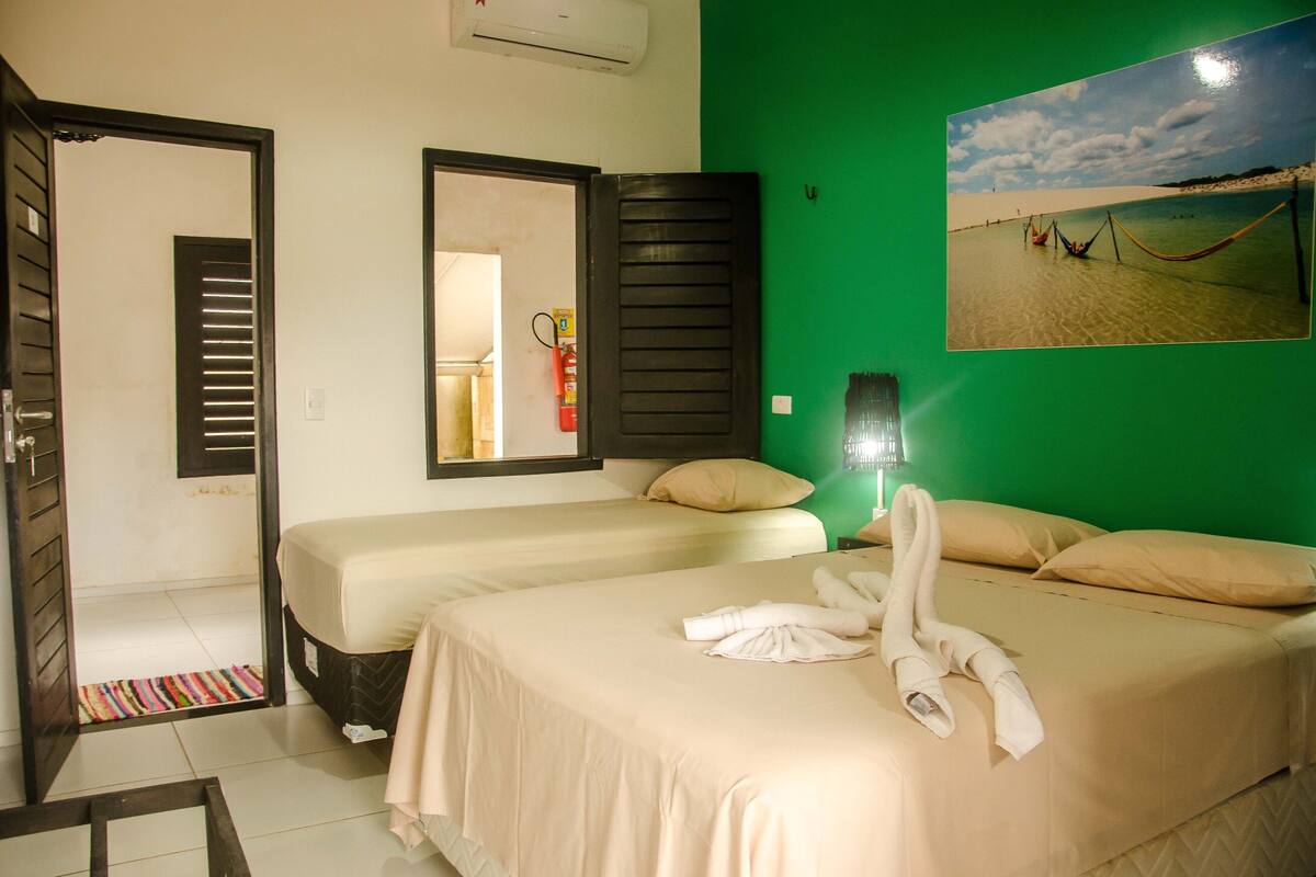 A hotel room with two beds, a green wall, a beach photo, and a fire extinguisher.