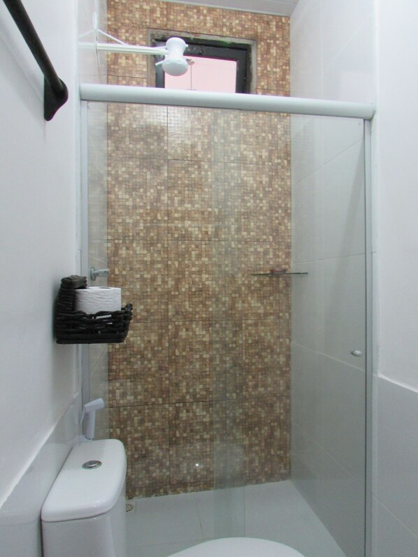 A bathroom with a shower, toilet, and a shelf with toiletries.