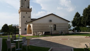 A building with a tower and a patio area with outdoor seating. - La Vecchia Torre (San Nicola Manfredi)