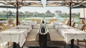 A restaurant with outdoor seating overlooking a lake, featuring tables with white tablecloths and wicker chairs. - La Réserve (Knokke-Heist)