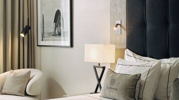 Una habitación de hotel moderna con una cama grande, una silla, un cuadro en la pared y una mesita de noche con una lámpara.