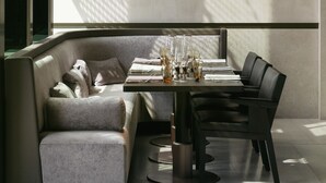 A modern dining area with a high table, chairs, and a cushioned bench. - La Réserve (Knokke-Heist)