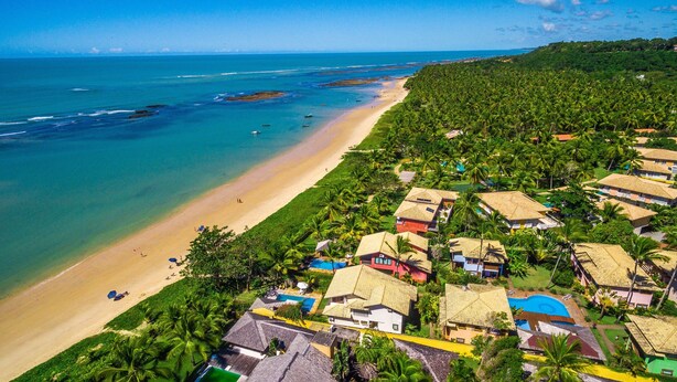 An aerial view of a coastal resort with beachfront properties, a sandy beach, and a clear view of the ocean. - Residence Pé na Areia (Porto Seguro)