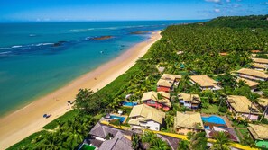 An aerial view of a coastal resort with beachfront properties, a sandy beach, and a clear view of the ocean. - Residence Pé na Areia (Porto Seguro)