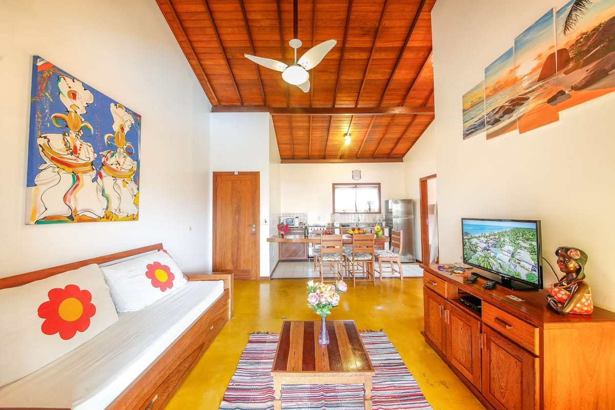 Una sala de estar con sofá, televisor, aparador de madera y obras de arte en las paredes.
