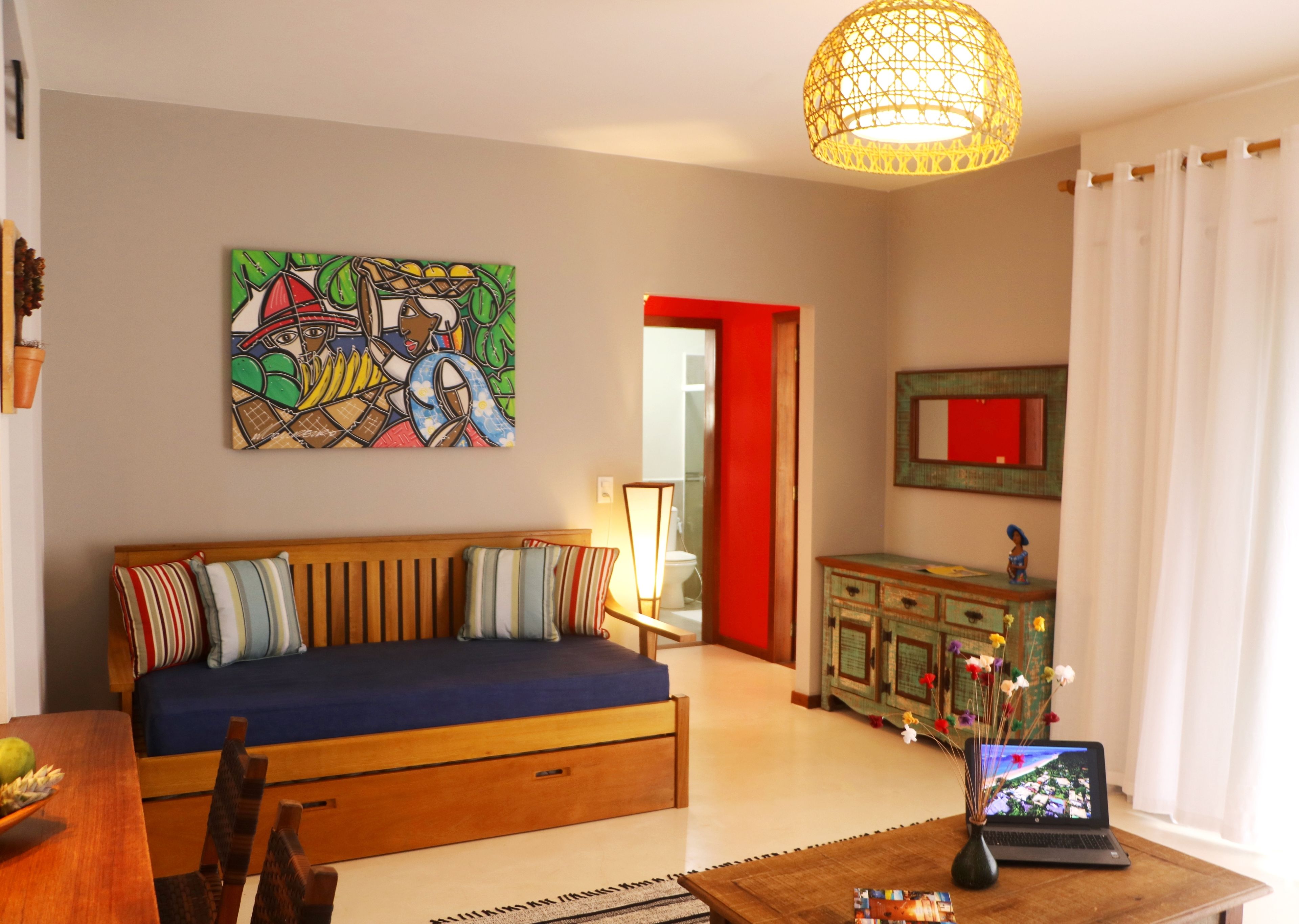 A living room with a sofa, a table with a laptop, a painting on the wall, and a cabinet with decorative items.