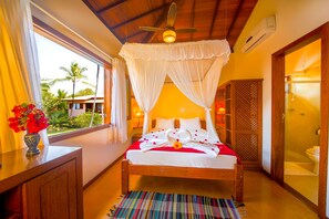 A bedroom with a bed, a ceiling fan, a window with curtains, and a view of palm trees. - Residence Pé na Areia (Porto Seguro)