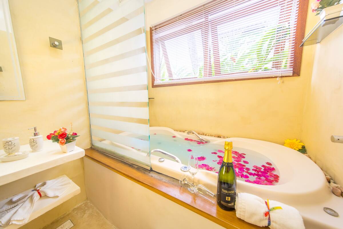 Un baño con una bañera llena de agua y pétalos de rosa, una botella de champán y una ventana con persianas.