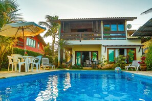 A two-story house with a swimming pool, outdoor furniture, and lush greenery. - Residence Pé na Areia (Porto Seguro)