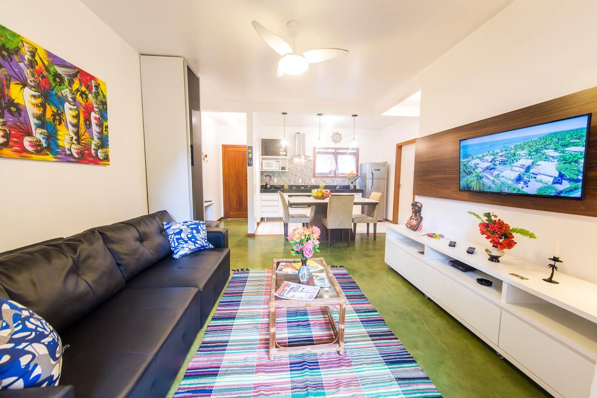 Una sala de estar moderna con un sofá negro, una alfombra colorida y un televisor montado en la pared.