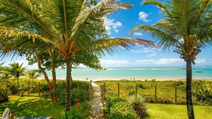 A tropical garden leading to a beach with palm trees and a clear view of the ocean. - Residence Pé na Areia (Porto Seguro)