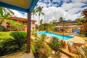 A pool area with lounge chairs, a hammock, and a small building with a blue awning. - Residence Pé na Areia (Porto Seguro)