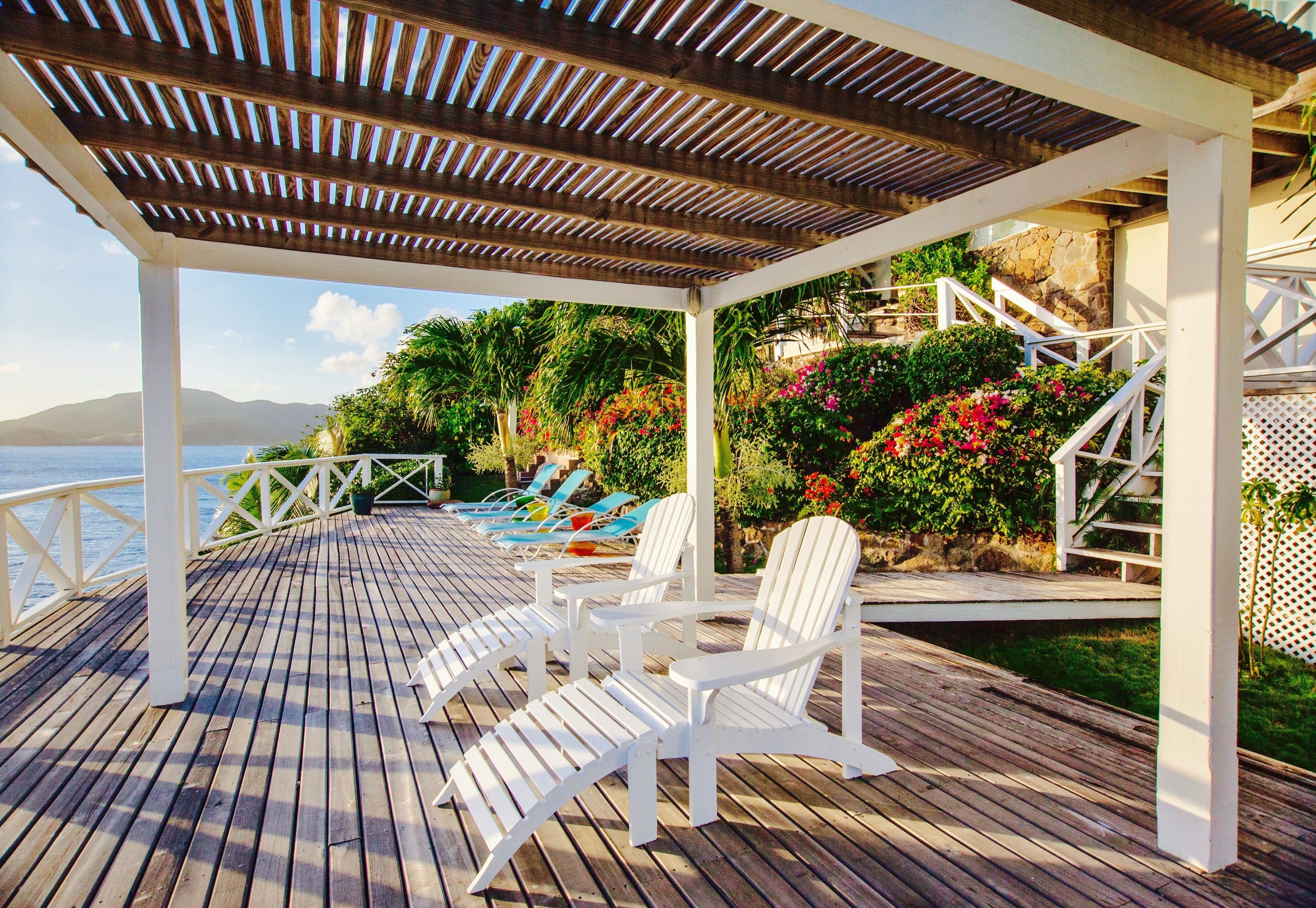 A wooden deck with white chairs and a view of the sea.