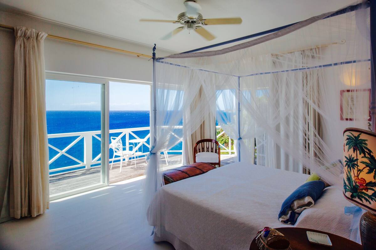 A room with a bed, a ceiling fan, and a view of the ocean.