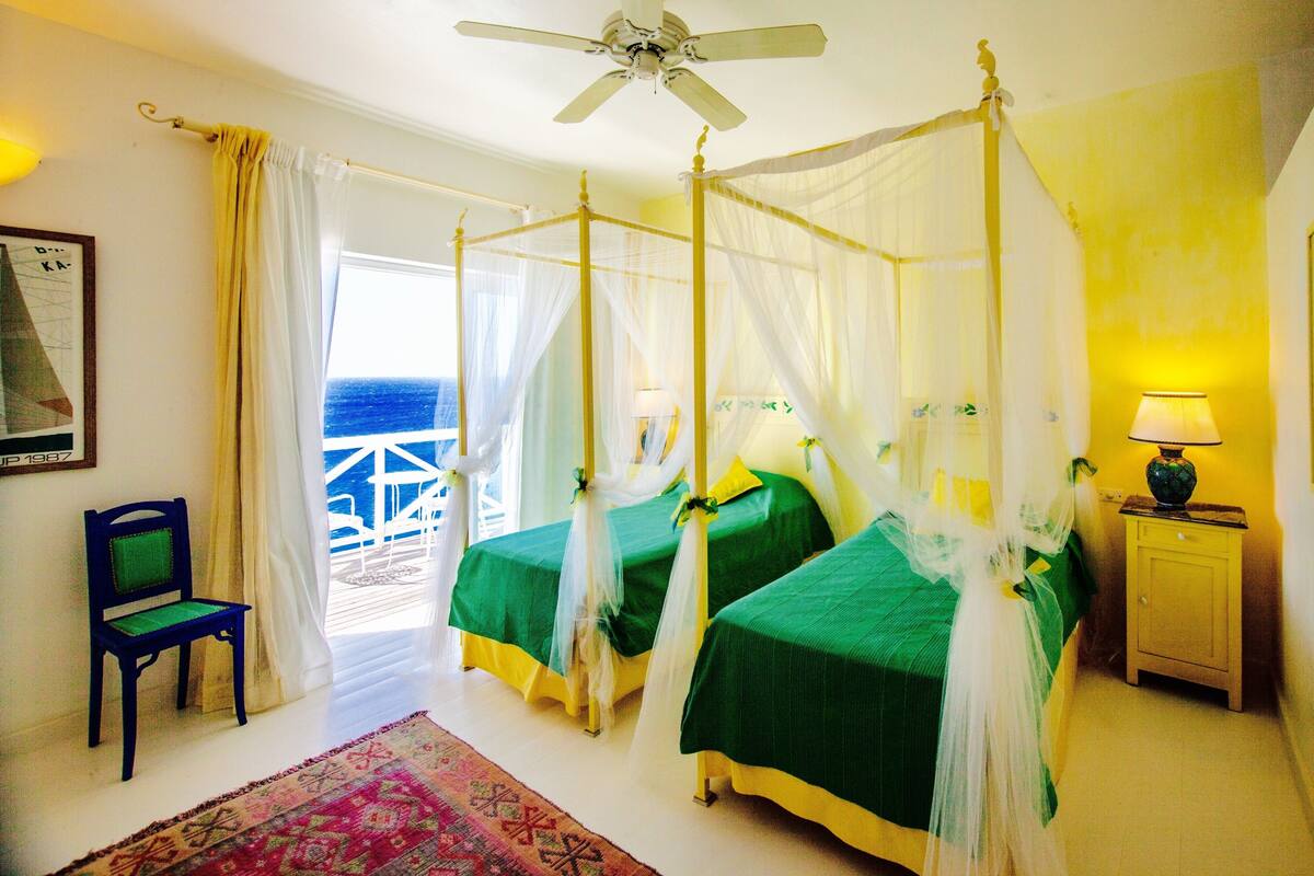 A four-poster bed with a canopy, two bedside tables, a chair, and a view of the sea.