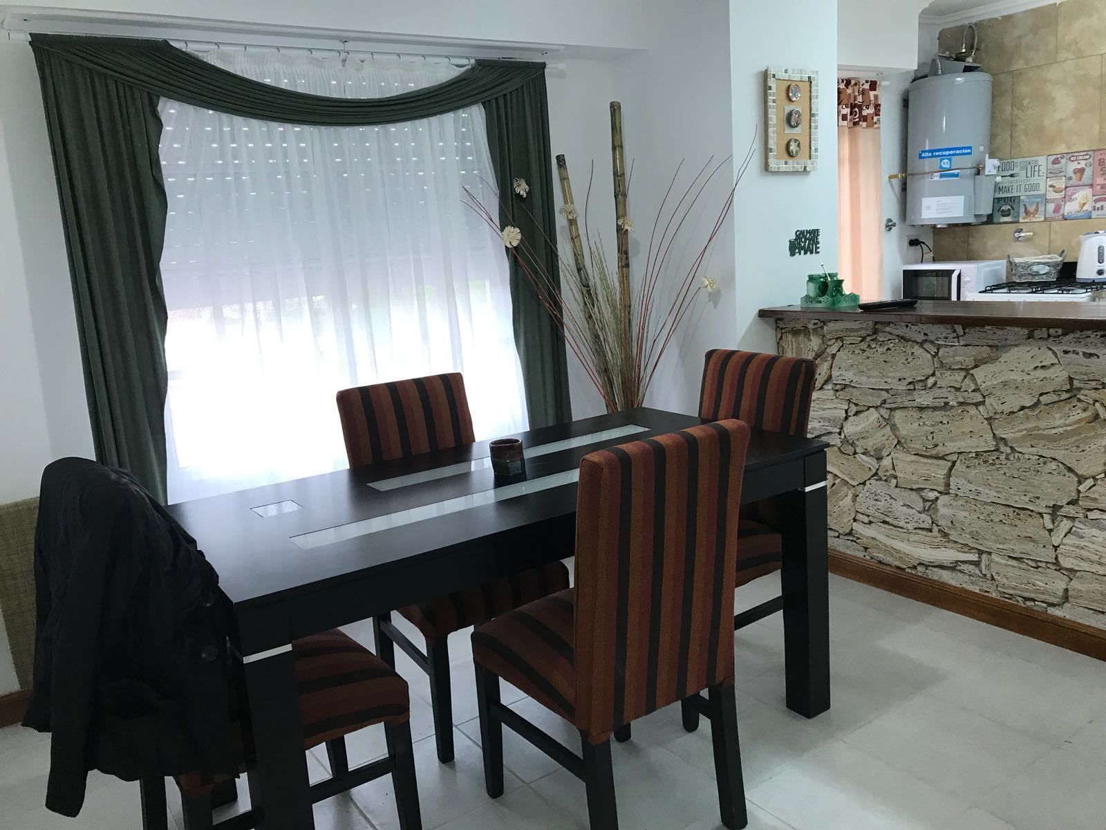 A dining area with a table and chairs, a kitchen area with a stone wall, and a window with curtains.