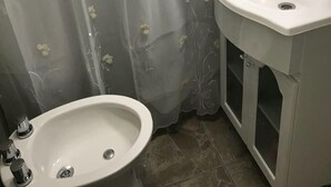 Casa de banho com lavatório branco, bidé e cortina de chuveiro com motivos florais.