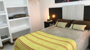 A bedroom with a bed, a nightstand, a shelf unit, and a painting on the wall.