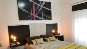 Cama bem arrumada com manta listrada, duas luminárias de cabeceira e uma pintura abstrata moderna acima.