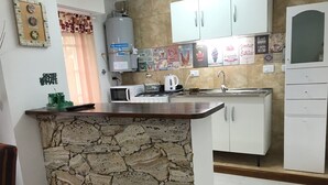 Cozinha com ilha de pedra, armários brancos, aquecedor, micro-ondas e diversos eletrodomésticos.