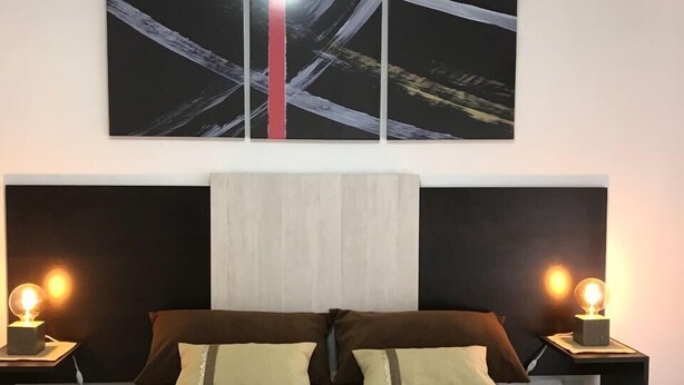 Quarto moderno com cama grande, duas mesas de cabeceira com abajures e um quadro abstrato grande acima da cama.